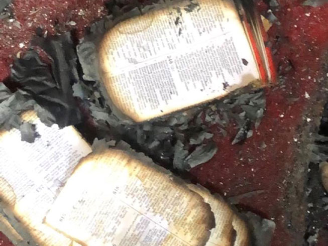Pages of burned Bible strewn across floor of ruined church